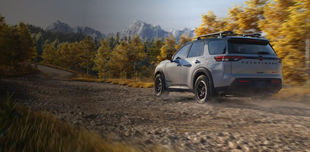 2026 Nissan Pathfinder rear view driving on a gravel road through autumn forest