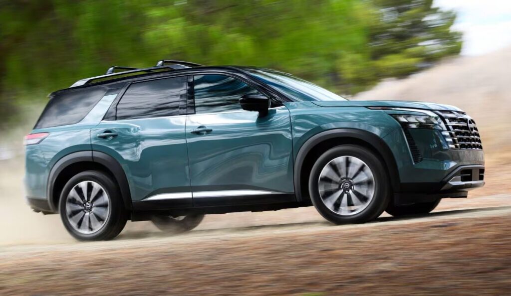 2026 Nissan Pathfinder side view driving on a dirt road past trees